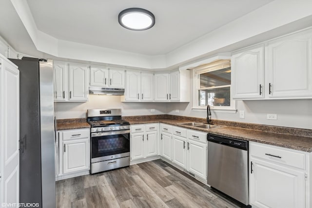 kitchen featuring under cabinet range hood, stainless steel appliances, dark wood-type flooring, a sink, and dark countertops