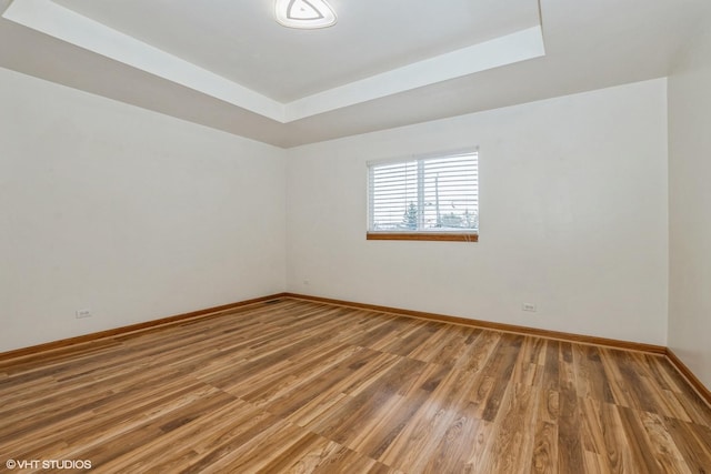 empty room featuring light wood-type flooring, a raised ceiling, and baseboards