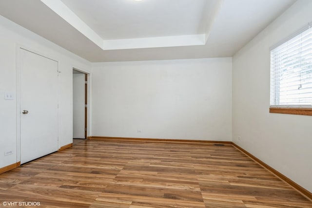 unfurnished room with a tray ceiling, baseboards, and wood finished floors