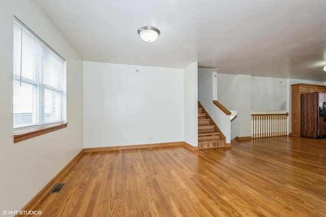 empty room with light wood-type flooring, stairway, baseboards, and visible vents