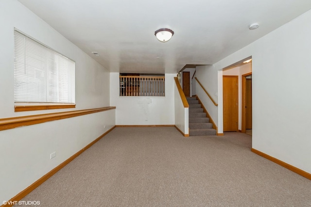 carpeted empty room with stairs and baseboards