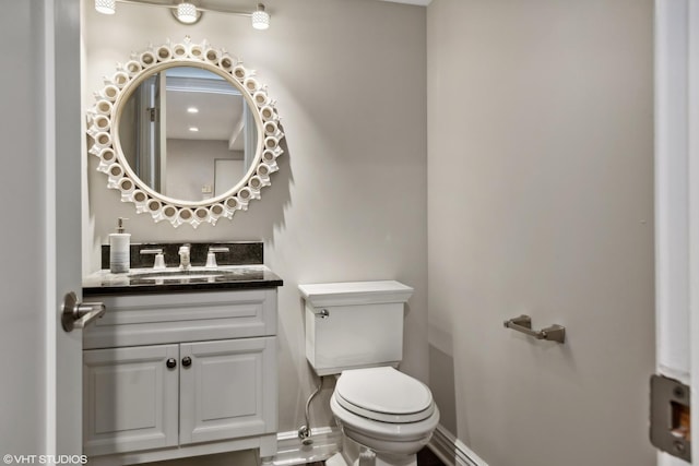 half bath with baseboards, vanity, and toilet