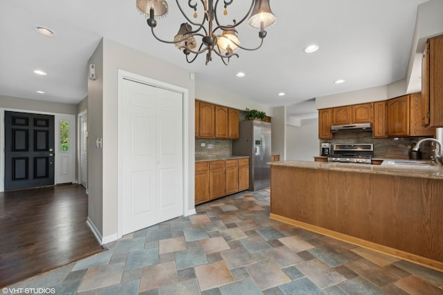 kitchen featuring under cabinet range hood, stove, a sink, stainless steel refrigerator with ice dispenser, and brown cabinetry