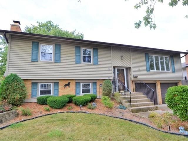 split foyer home featuring brick siding, a garage, and a chimney