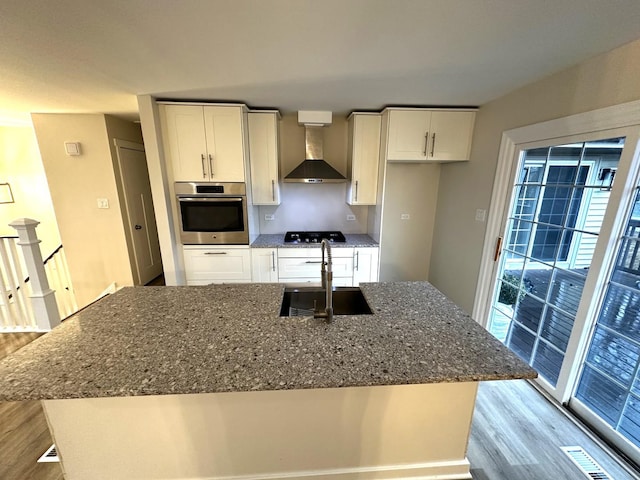 kitchen featuring gas cooktop, wood finished floors, a sink, stainless steel oven, and wall chimney range hood