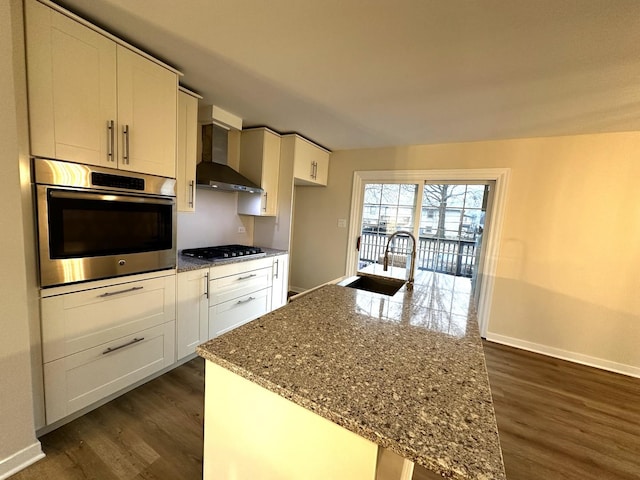 kitchen featuring dark wood-type flooring, a sink, gas stovetop, wall chimney exhaust hood, and stainless steel oven