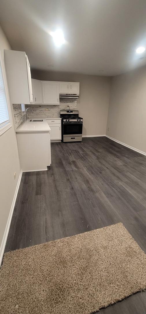 kitchen featuring dark wood-style floors, white cabinetry, light countertops, backsplash, and stainless steel gas stove