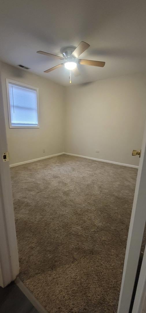 carpeted spare room featuring a ceiling fan, visible vents, and baseboards