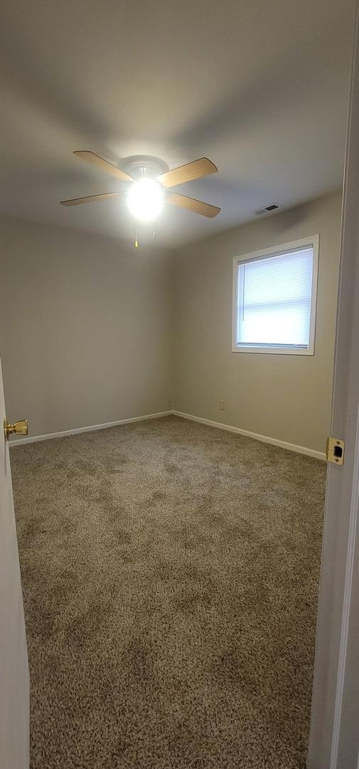 carpeted empty room featuring baseboards, visible vents, and a ceiling fan