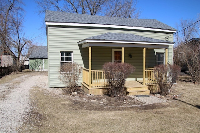 view of front of home with dirt driveway, a porch, and roof with shingles