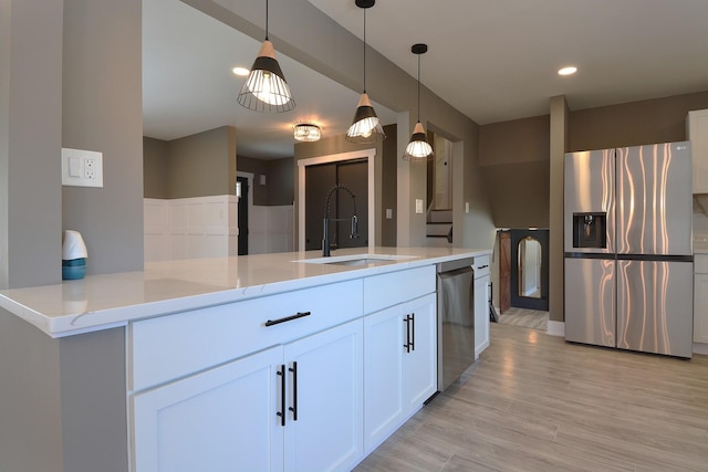 kitchen featuring stainless steel appliances, light stone counters, a sink, and white cabinetry