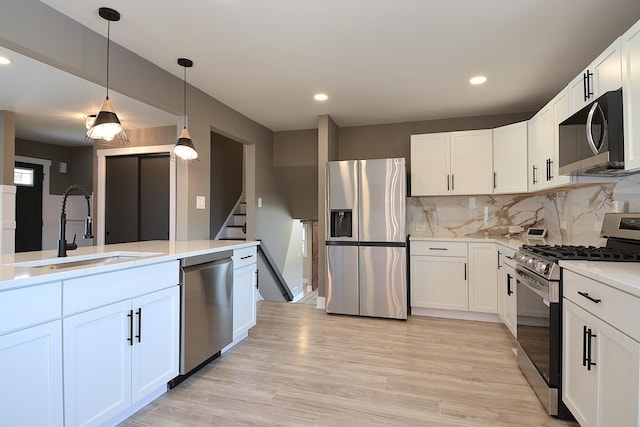 kitchen featuring stainless steel appliances, light countertops, backsplash, light wood-style floors, and a sink