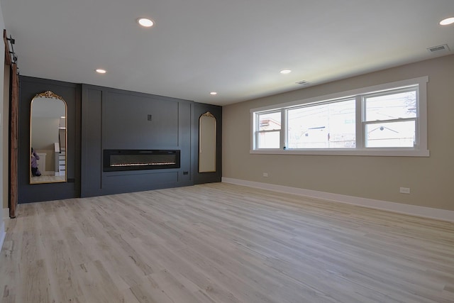 unfurnished living room featuring a barn door, recessed lighting, a large fireplace, visible vents, and light wood-type flooring