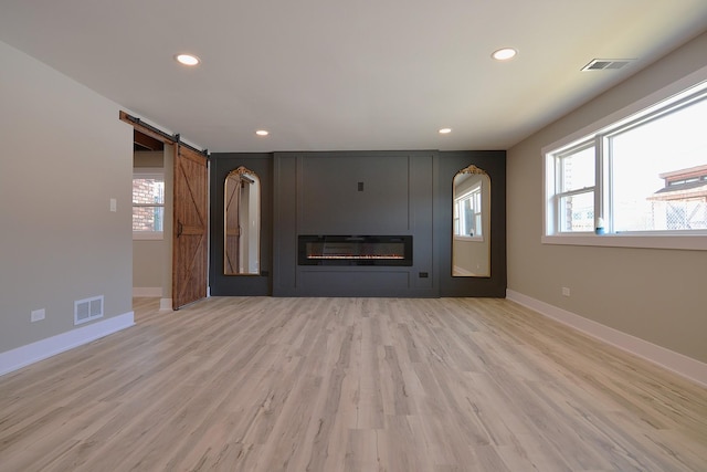 unfurnished living room with light wood-type flooring, a large fireplace, visible vents, and a barn door