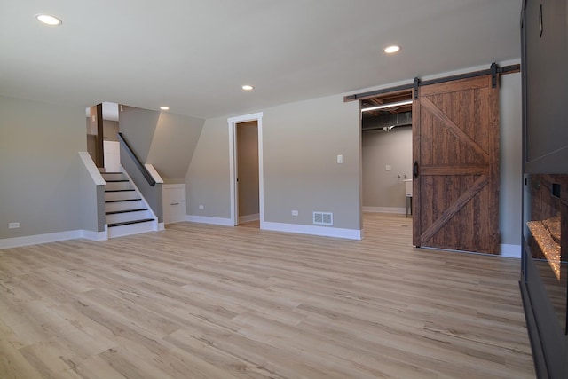 basement featuring light wood finished floors, a barn door, stairs, and visible vents