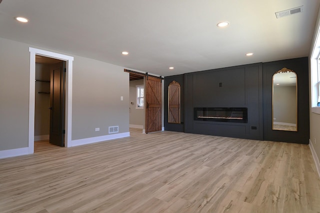 unfurnished living room featuring a barn door, light wood-style floors, visible vents, and recessed lighting