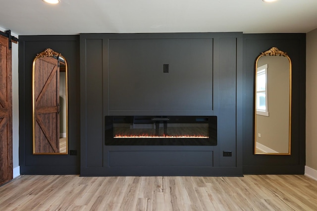 interior details featuring wood finished floors, a barn door, a glass covered fireplace, and baseboards