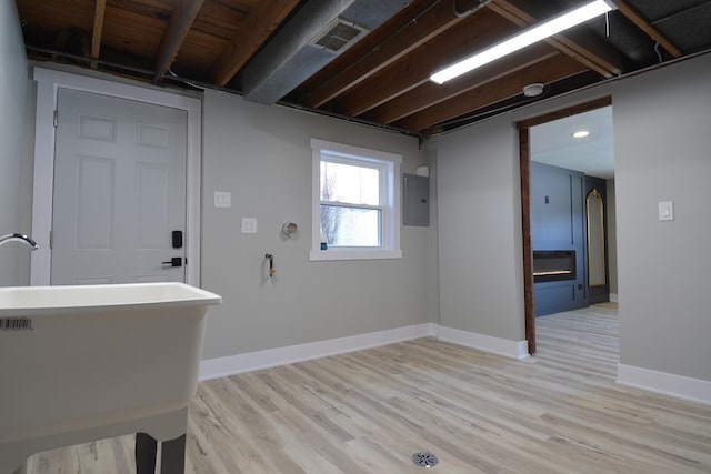 interior space featuring light wood finished floors, electric panel, baseboards, and a sink