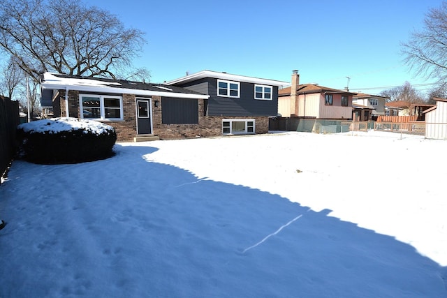 snow covered back of property with fence and brick siding