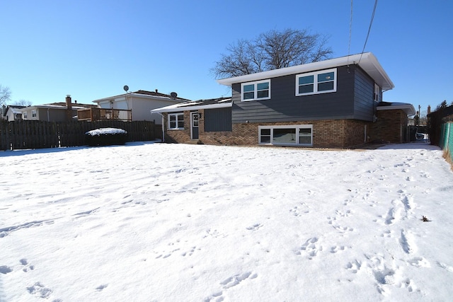 snow covered rear of property featuring fence and brick siding