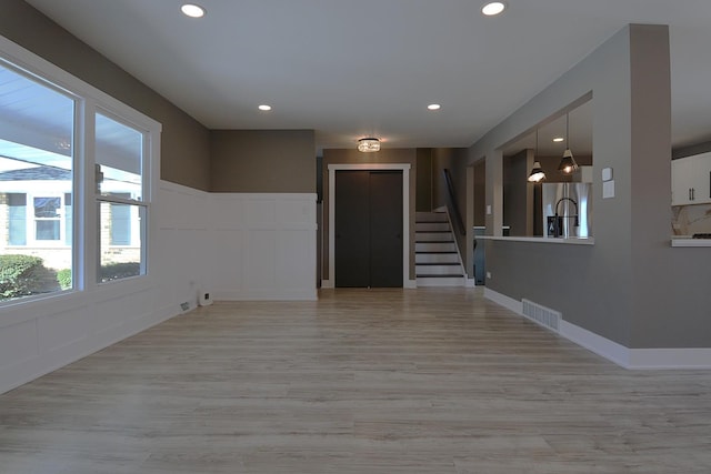 empty room featuring stairway, visible vents, a decorative wall, and light wood-style floors