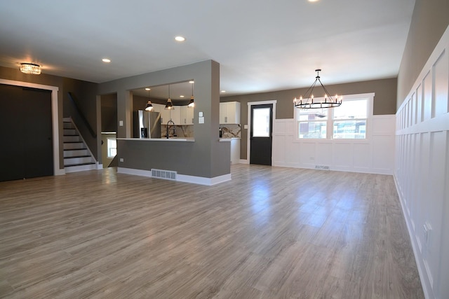 unfurnished living room with light wood-style flooring, recessed lighting, visible vents, stairway, and an inviting chandelier