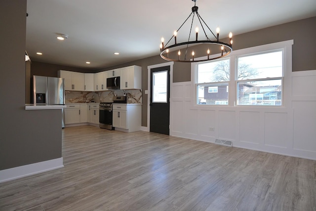 kitchen featuring visible vents, white cabinets, stainless steel appliances, light wood-style floors, and a decorative wall