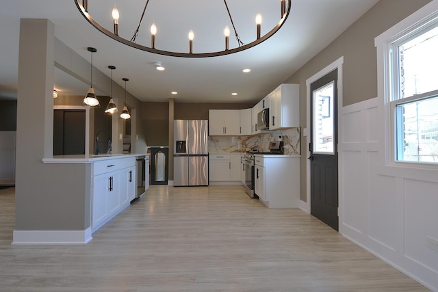 kitchen with decorative light fixtures, light countertops, a decorative wall, decorative backsplash, and appliances with stainless steel finishes