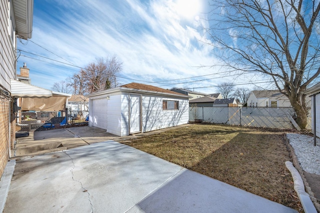 view of yard featuring a garage, concrete driveway, a patio, a fenced backyard, and an outbuilding