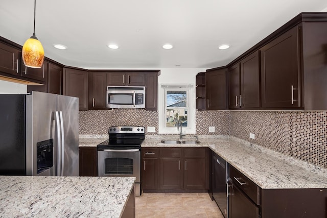 kitchen featuring dark brown cabinetry, appliances with stainless steel finishes, hanging light fixtures, light stone countertops, and a sink