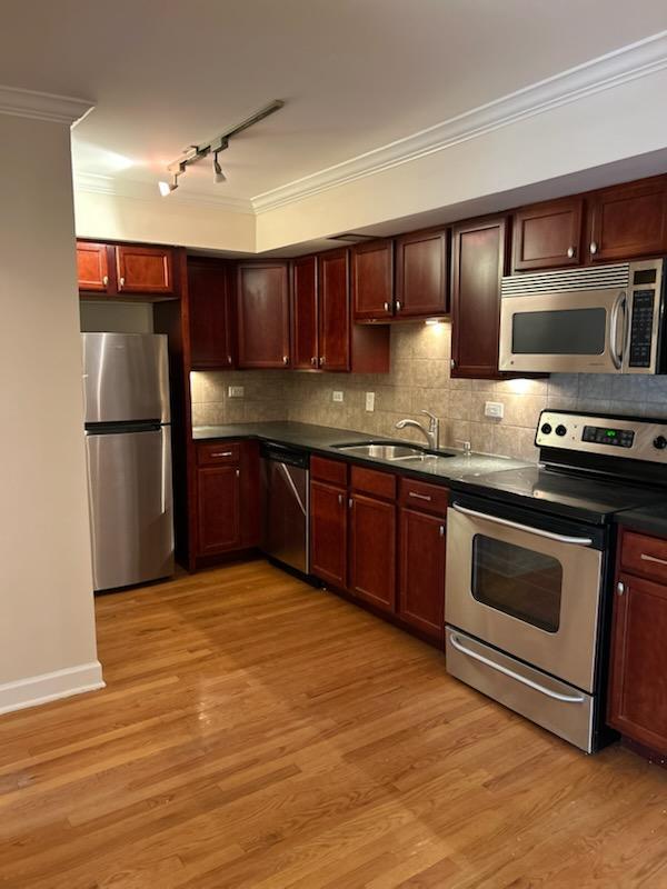 kitchen with light wood-type flooring, ornamental molding, a sink, tasteful backsplash, and appliances with stainless steel finishes