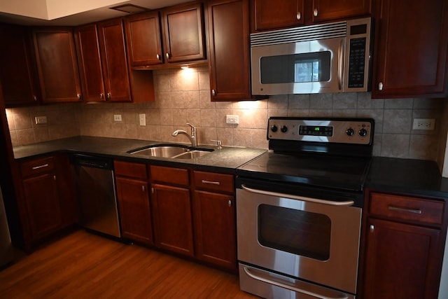 kitchen featuring light wood-style flooring, a sink, backsplash, dark countertops, and appliances with stainless steel finishes