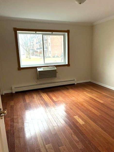 unfurnished room featuring wood finished floors, baseboards, ornamental molding, an AC wall unit, and baseboard heating