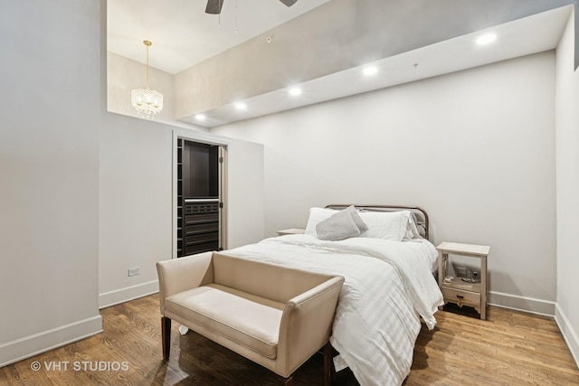 bedroom with light wood-style flooring, ceiling fan with notable chandelier, baseboards, and recessed lighting