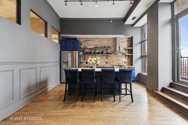 bar with plenty of natural light, stainless steel fridge, a decorative wall, and wall chimney range hood