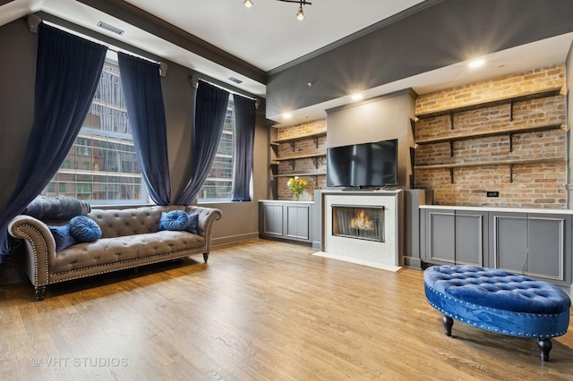 living area featuring visible vents, built in features, brick wall, a fireplace with flush hearth, and wood finished floors