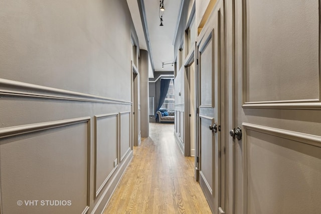 corridor featuring a decorative wall, light wood-style flooring, and track lighting