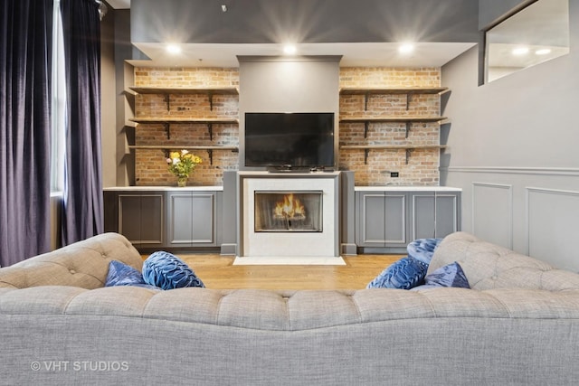 living area with a fireplace with flush hearth, wainscoting, wood finished floors, and a decorative wall