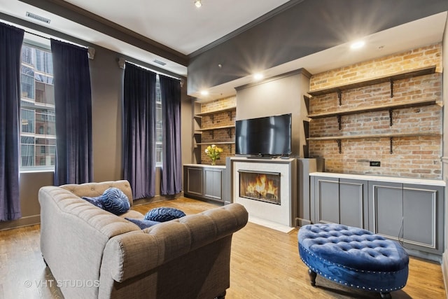 sitting room featuring built in shelves, crown molding, a fireplace with flush hearth, brick wall, and wood finished floors