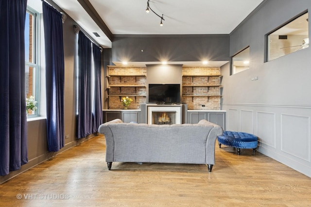 living area featuring a decorative wall, ornamental molding, track lighting, wood finished floors, and a warm lit fireplace