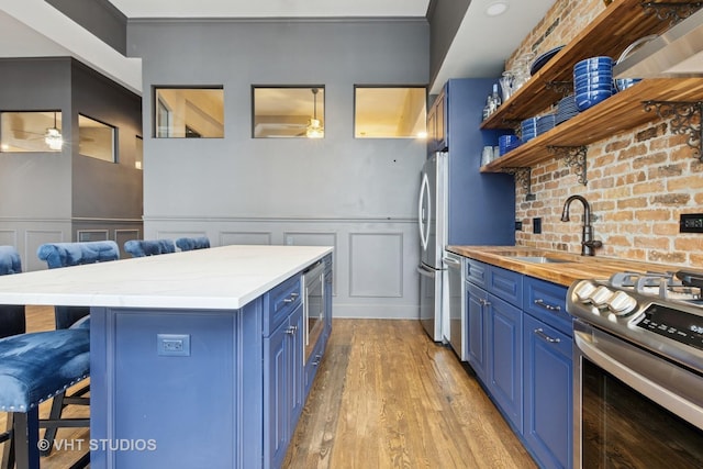 kitchen with ceiling fan, appliances with stainless steel finishes, blue cabinetry, a kitchen bar, and a sink