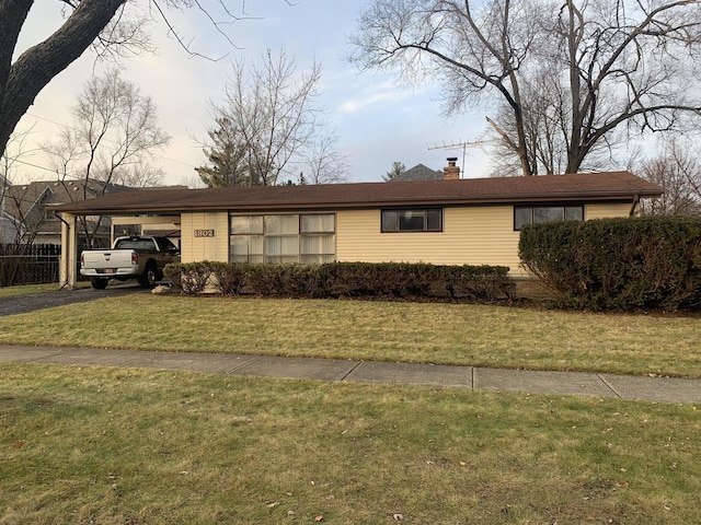 single story home featuring a chimney, aphalt driveway, a carport, and a front yard