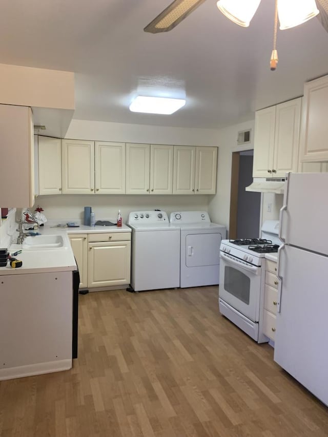 kitchen with light wood-style flooring, under cabinet range hood, white appliances, a sink, and washing machine and clothes dryer