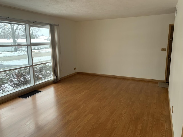 empty room featuring light wood-type flooring, visible vents, a textured ceiling, and baseboards