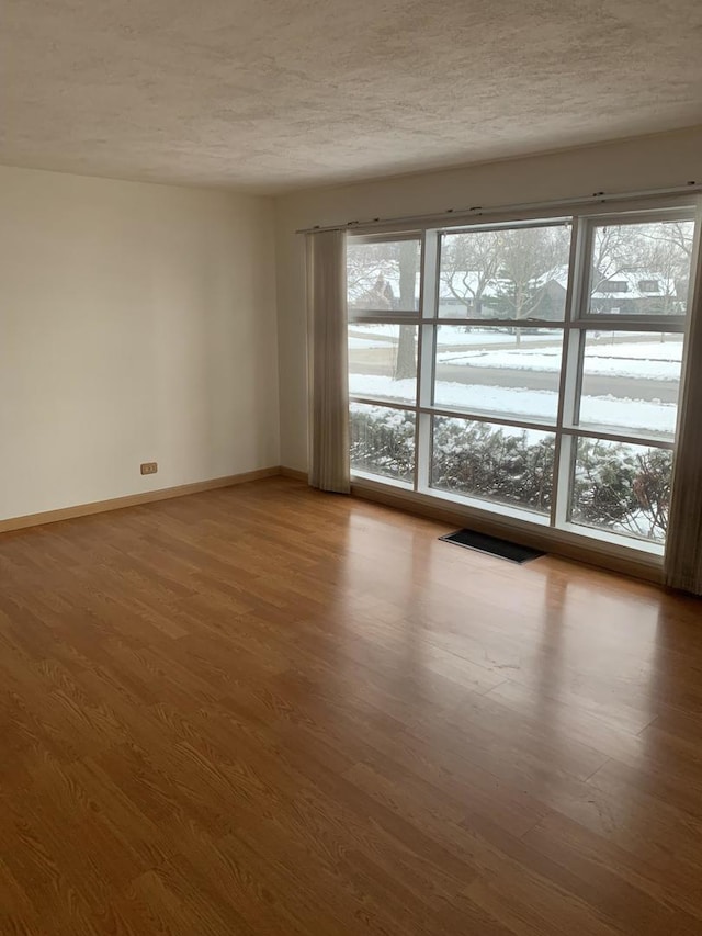 spare room featuring a textured ceiling, wood finished floors, and baseboards