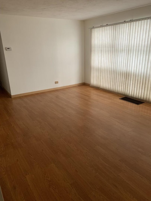 spare room featuring visible vents, baseboards, and wood finished floors