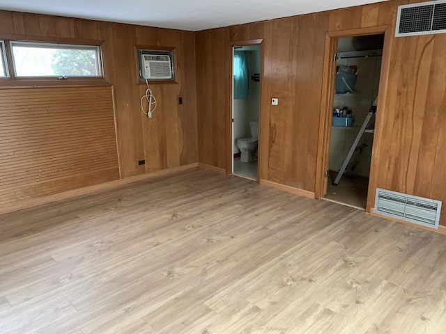 unfurnished room featuring an AC wall unit, visible vents, wood walls, and wood finished floors