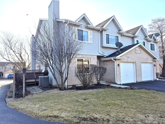 view of front of house featuring brick siding, a front lawn, central AC, a chimney, and driveway