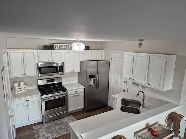 kitchen with a sink, a peninsula, white cabinets, stainless steel appliances, and dark wood-style flooring