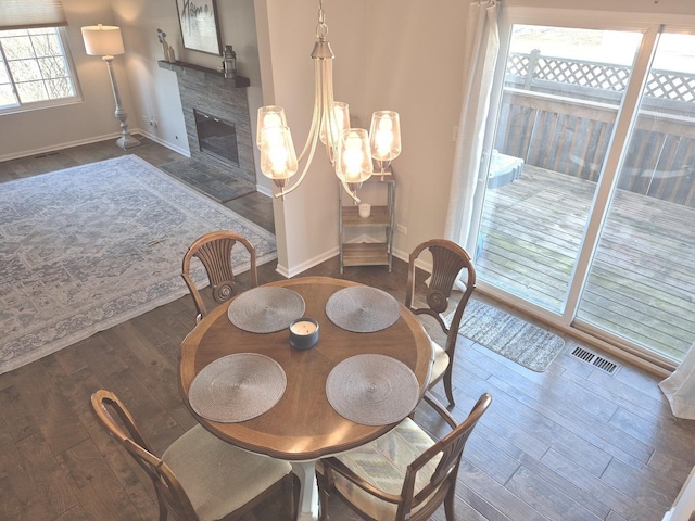 dining space featuring visible vents, a stone fireplace, baseboards, and hardwood / wood-style floors